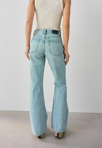 Lichtblauwe spijkerbroek met flare en hoge taille, met achterzakken en subtiele vervaging, gecombineerd met gepatternde hoge hakken.