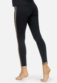 Czarne legginsy wykonane z elastycznego materiału, z metalicznymi złotymi paskami po bokach i złotymi akcentami przy kostce. Lekka i dopasowana konstrukcja.
