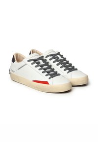 Baskets blanches en cuir avec des lacets gris, un talon gris et des accents rouges. Elles disposent d'une semelle texturée et d'un design minimaliste.