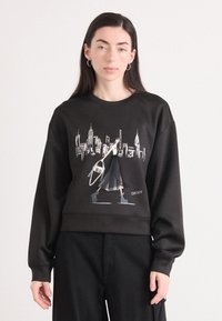 Sweatshirt preto com um design gráfico de um horizonte urbano e uma figura a carregar uma mala. Apresenta um corte descontraído, gola redonda e textura suave.