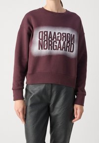 Sweatshirt courte couleur marron avec une impression graphique portant le texte "Nørgaard" en couleurs contrastées. Présente une coupe décontractée et des poignets côtelés.