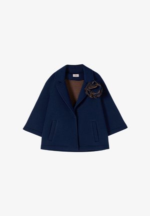 Laivastonsininen lyhyt takki leveillä hihoilla, kapeilla kauluskäänteillä, kahdella etutaskulla, raidallisella vuorauksella ja raidallisella kangaskukkanappineulalla kauluskäänteessä.