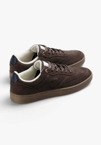 Bruna mockaskor med vit foder och mörkblå häldetaljer. Har rund snörning, en texturerad gummisula och subtil logotyp.