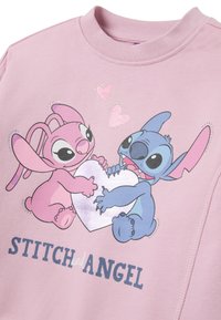Sudadera rosa con personajes animados Stitch y Angel sosteniendo un corazón, con acentos brillantes y "STITCH y ANGEL" impreso debajo.