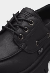 Μαύρο δερμάτινο παπούτσι με κορδόνια, μεταλλικές οπές, εμφανές ετικέτα με το λογότυπο Buffalo και υφασμένο χοντρό πέλμα.