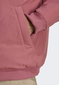 Ljusrosa jacka med ribbade ärmslut och nederkant, slätt tyg, sidoficka med klaff och en avslappnad passform.