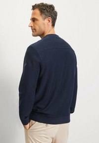 Marineblauwe sweatshirt met lange mouwen, ribgebreide manchetten en een ronde halslijn. Heeft een subtiele textuur en een logo-accent op de linkerschouder.