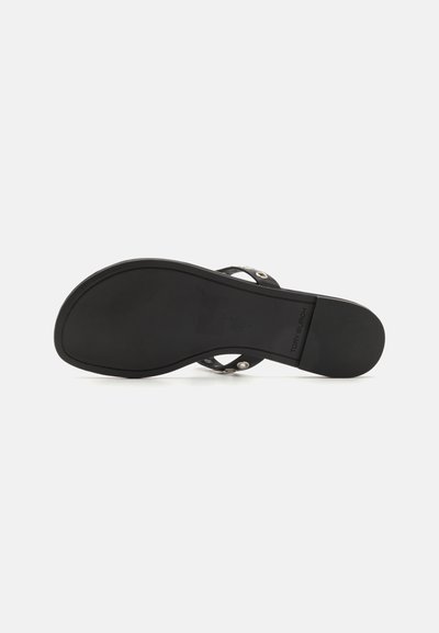 Tongs noires avec une semelle plate, dotées d'un fond texturé, d'un design à brides croisées et d'accents en métal circulaires.