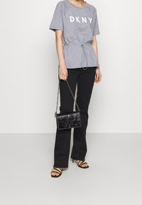Camisa corta de manga gris con estampado "DKNY" y cintura con cordón, combinada con pantalones acampanados negros y un bolso de cuero negro para el hombro.