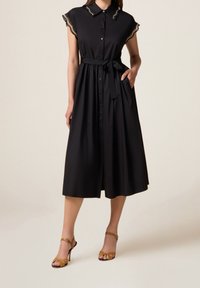 Robe midi noire à manches courtes, avec une patte de boutonnage à l'avant, une ceinture à la taille et des détails en dentelle au col. Tissu lisse, silhouette trapèze.
