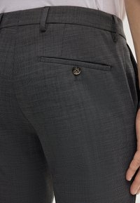 Dunkelgraue, maßgeschneiderte Hose aus strukturiertem Stoff, mit einer einzelnen, per Knopf gesicherten Gesäßtasche und einem flachen Vorderdesign.