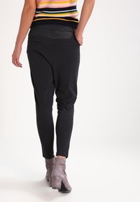 Zwarte joggingsbroek met een taps toelopend ontwerp, elastische tailleband en voorkeurszakken, gecombineerd met grijze enkellaarzen. Stevige stoftextuur.