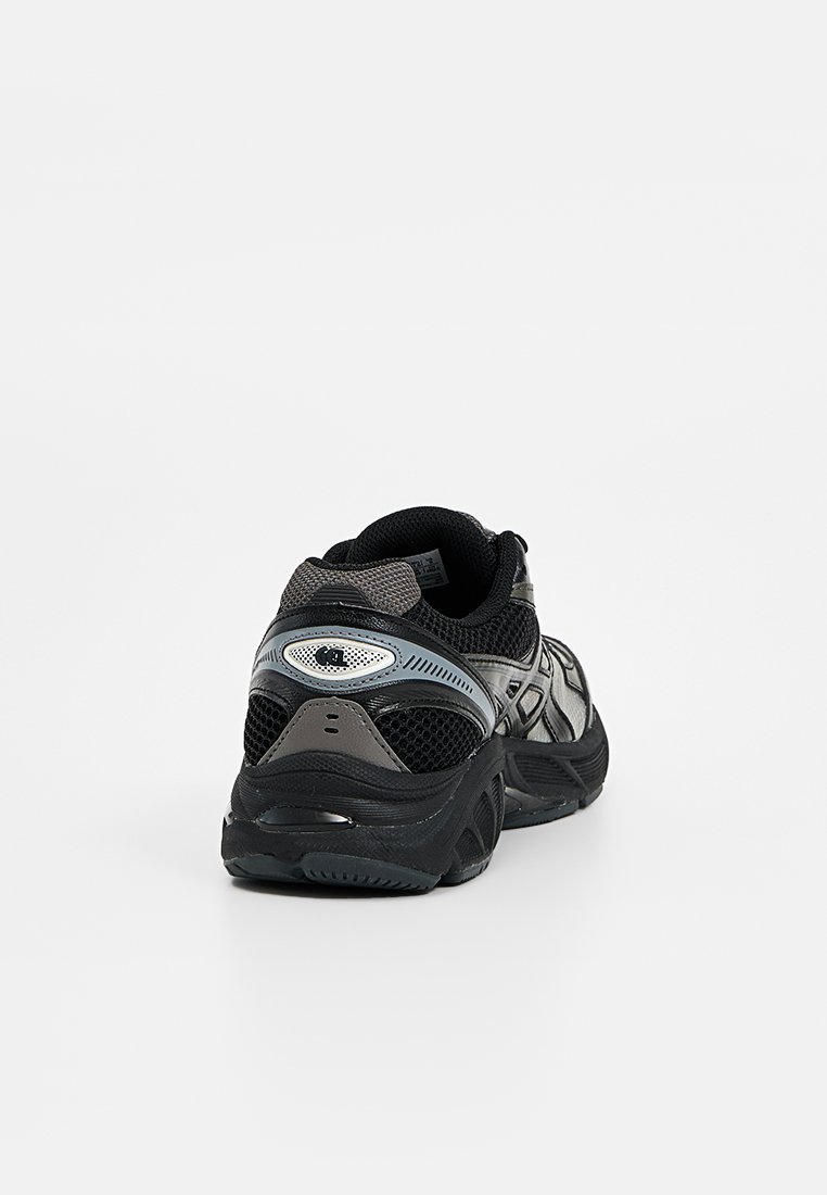 Baskets de sport noires et grises avec des panneaux en mesh et une semelle épaisse, vues de l'arrière sur fond blanc uni.