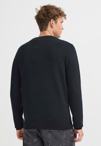 Mørk marineblå strikkegenser med lange ermer, ribbestrikkede mansjetter og nederkant, samt rund halslinning. Glatt tekstur uten synlige mønstre eller tilbehør.