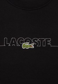 Sudadera de algodón negra con el texto "LACOSTE" bordado en blanco y un logo de cocodrilo verde. Textura suave con un diseño de cuello redondo.