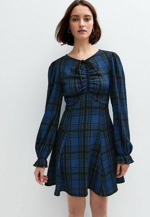 Vestido a cuadros azul y negro con mangas largas abullonadas, detalle fruncido en la parte delantera y neckline con lazo. Tejido suave con una textura lisa.