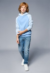 Sweatshirt com capuz azul claro, com bolso canguru e mangas contrastantes. Usado com jeans azuis desbotados e sapatilhas brancas.
