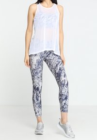 White sleeveless mesh tank top over gray and navy patterned leggings; silver athletic shoes with textured detailing.