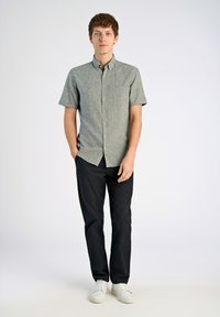 Korte mouwen, knoopsluiting blouse in lichtgrijze stof met een gestructureerde afwerking. Gecombineerd met donkere broeken en witte sneakers.