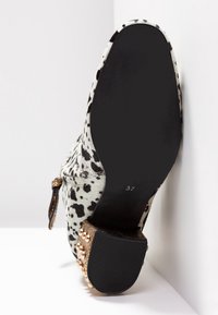 Buty na obcasie z białą i czarną plamkowaną fakturą, ozdobione złotymi akcentami na obcasie. Rozmiar oznaczony jako 37 na podeszwie.