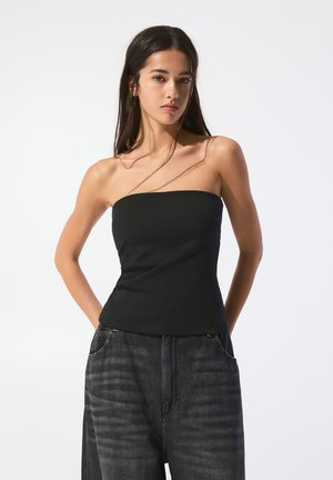 Top noir sans bretelles au design ajusté, en tissu lisse. Assorti à un pantalon en denim ample avec un motif rayé subtil.