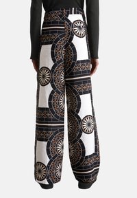 Pantaloni a gamba ampia con un motivo geometrico in nero, bianco e ruggine. Tessuto in cotone con una texture liscia e design a vita alta.