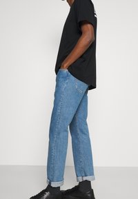 Camiseta de algodón negra de manga corta combinada con jeans de mezclilla azul claros. Los jeans son ligeramente ajustados con puños enrollados. Zapatos negros.