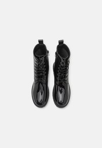 Botines de charol negro con un acabado brillante, cordones frontales y cremallera lateral. Presentan punteras redondas y suelas texturizadas.