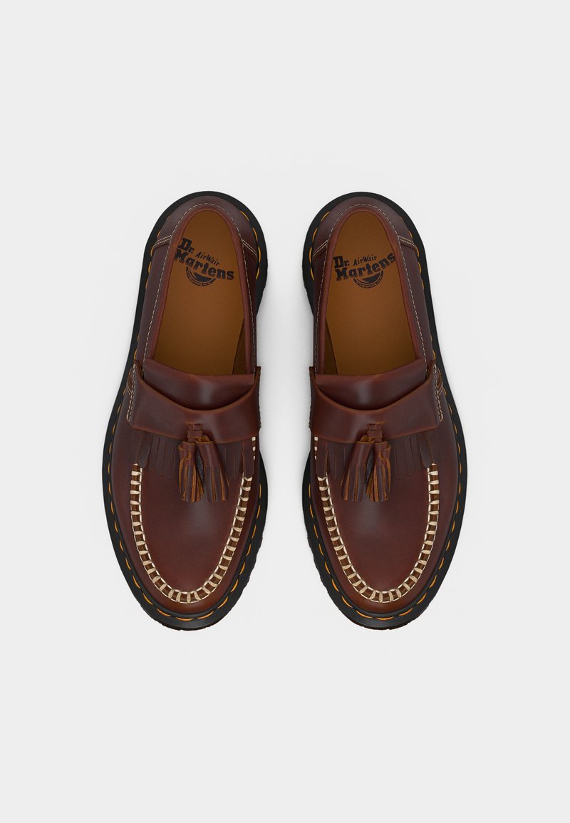 Coppia di mocassini marroni in pelle con nappine, frange, cuciture a contrasto e suole nere con cuciture gialle, marchio Dr. Martens all'interno.