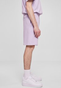 Lilla bomullsshorts med elastisk midje og sidelommer, kombinert med hvite joggesko og matchende ankelsokker.