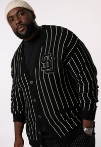 Zwart-wit gestreepte cardigan met V-hals, knoopsluiting en logo patch. Gemaakt van gebreide stof met een ontspannen pasvorm.