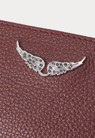 Piele texturată burgundy cu un ornament în formă de aripă argintie, având detalii complexe și pietre negre. Cusut cu grijă pe margine.