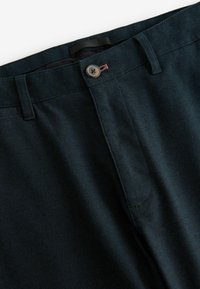 Mørkegrønne kordfløjspants med knaplukning, robust talje og fin ribbet tekstur, der fremviser nærbilleder af stof og syninger.