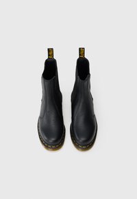 Botas de tornozelo em couro preto com um acabamento texturizado, painéis laterais elásticos, costura amarela e puxadores com a marca na parte de trás.