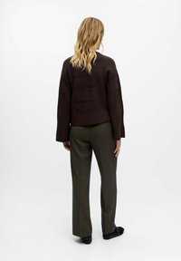 Bruine gestructureerde gebreide trui met een cropped ontwerp, gecombineerd met groene tailleursbroek. De outfit heeft lange mouwen en een relaxte pasvorm.