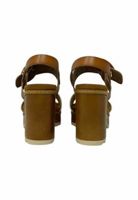 Sandali con tacco marroni, con ampie cinghie e chiusura a fibbia. Parte superiore texturizzata e base liscia. Tacchi spessi e solidi con un suola di colore chiaro.