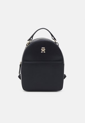 Black leather mini backpack with top handle, front pocket, gold hardware, and a small gold logo emblem at the center front.