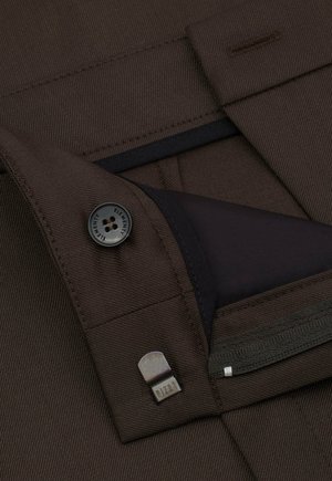 Brązowy materiał tekstylny o fakturowanym wykończeniu, z czarnym guzikiem oraz kieszenią na zamek z gładką, ciemną podszewką i metalicznym akcentem.