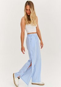 Lehké modro-bílé pruhované široké kalhoty se štěrbina, elastickým pasem a růžovými knoflíky, spárované s bílými teniskami.