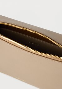 Μπεζ δερμάτινο πουγκί με φερμουάρ με χρυσά δόντια, μερικώς ανοιχτό, που δείχνει το λείο εσωτερικό και το λογότυπο Calvin Klein στο εσωτερικό.