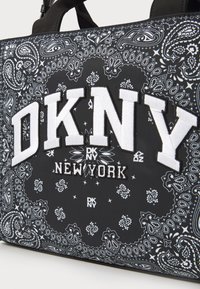 Sort stofpose med hvide paisley mønstre. Har et stort broderet "DKNY NEW YORK" logo, teksturerede accenter og subtile logodesigns.