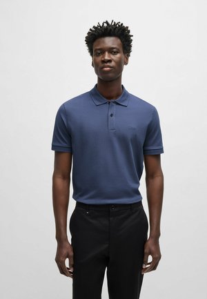 Marineblauwe polo shirt van zachte stof, met een klassieke kraag, korte mouwen en een subtiele logo op de borst. Gecombineerd met zwarte broek.