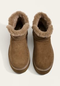 Hnedé semišové členkové topánky s umelou kožušinou na vrchu, zaoblené špičky a šitie pozdĺž podrážky. Rovná, protišmyková podrážka.
