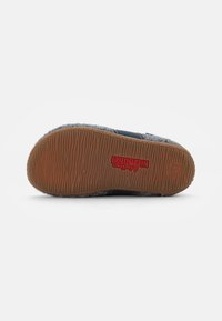 Calzature grigie con una tomaia testurizzata, dettagli blu scuro e suola flessibile in gomma marrone. Presenta un logo rosso sul lato della suola.