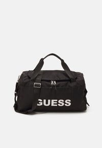 Borse da palestra in nylon nero con spallacci regolabili, grande logo bianco "GUESS", chiusura con doppia cerniera e dettagli di tasche laterali aggiuntive.
