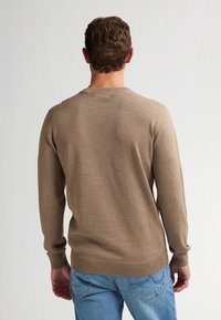 Pulover tricotat maro cu mâneci lungi, decolteu rotund și manșete cu nervuri, asortat cu blugi de culoare albastră deschisă. Textura pare moale și netedă.