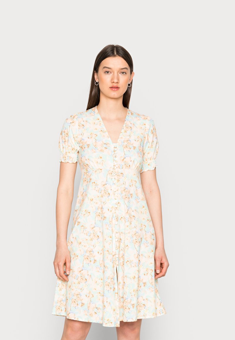 Vestido floral em azul claro, apresentando um decote em V, mangas curtas bufantes, detalhes em botões e uma saia godê com um tecido texturizado.