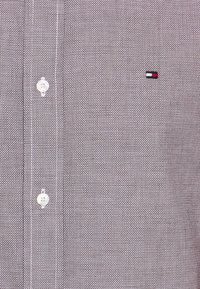 Gray button-up shirt with a textured pattern, featuring white buttons and a small logo in red, white, and blue.