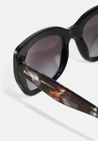 Mustat ylisuuria aurinkolaseja kiiltävällä pinnalla, harmaan sävyttävät linssit ja kilpikonnakuosiset sangaat, joissa on hopeisia brändiyksityiskohtia.