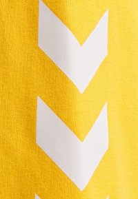 Tela amarilla con un patrón de grandes flechas blancas apuntando hacia abajo. La textura parece suave y de punto.